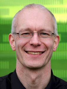 Matthias Vojta lächelt in die Kamera, vor grünem unscharfem Hintergrund.